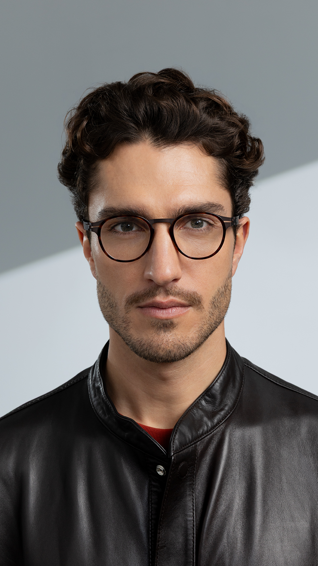 Man wearing OVVO Optics DUO Calvin round tortoiseshell eyeglasses and a black leather jacket against a gray background